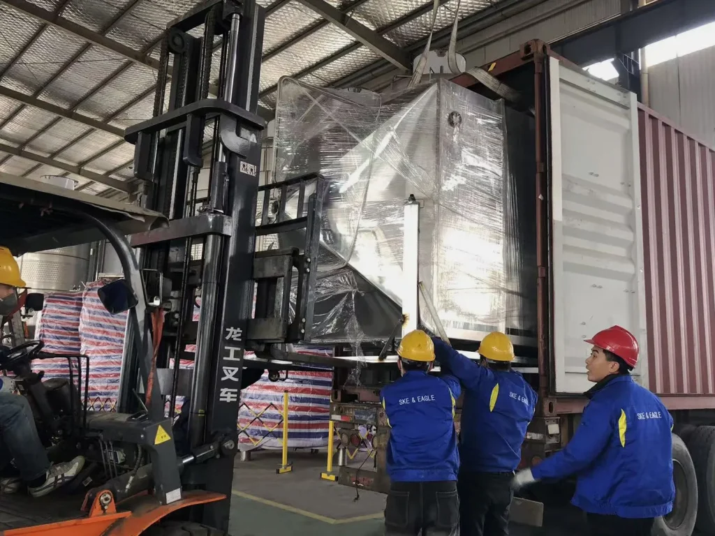 Workers positioning grain handling equipment beside a shipping container